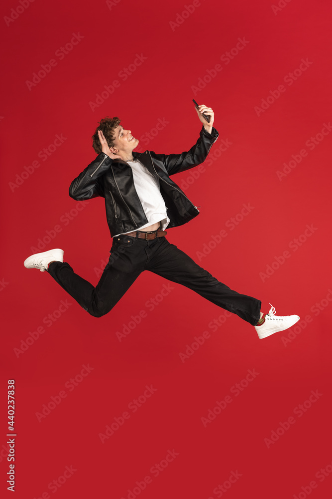 Always on mobile. Full length of young man taking phone while jumping against red studio background. Mobile, motion, movement, Always on mobile. Full length of young man taking phone while jumping against red studio background. Mobile, motion, movement,