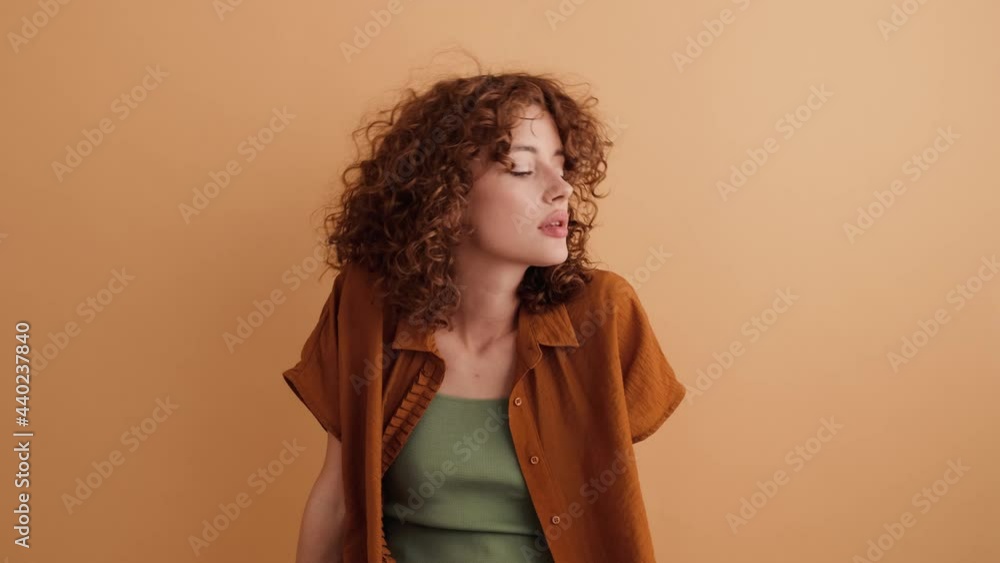 A calm pretty nice woman with curly hair is looking to the side standing isolated over a beige wall in the studio A calm pretty nice woman with curly hair is looking to the side standing isolated over a beige wall in the studio