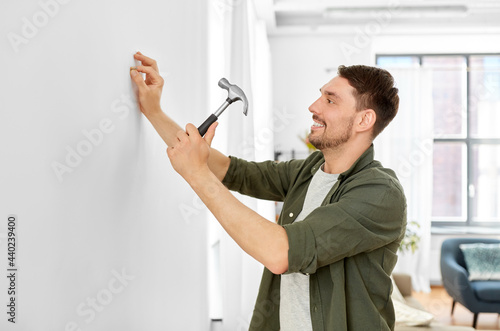 home improvement, repair and people concept - happy smiling man hammering nail to wall