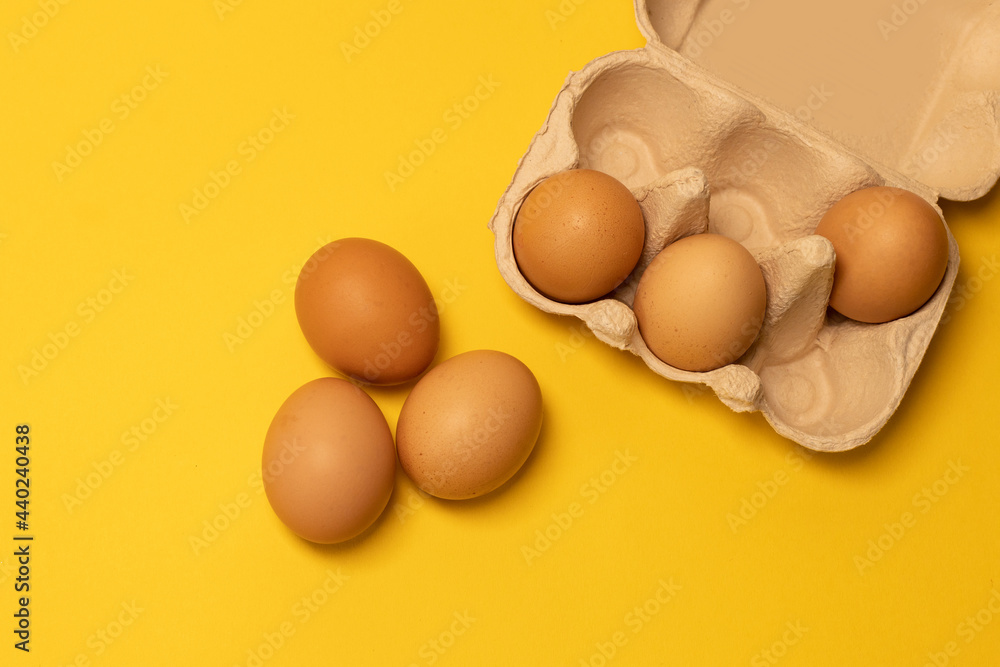 Brown chicken eggs and one broken egg with yolk in eco basket on yellow background