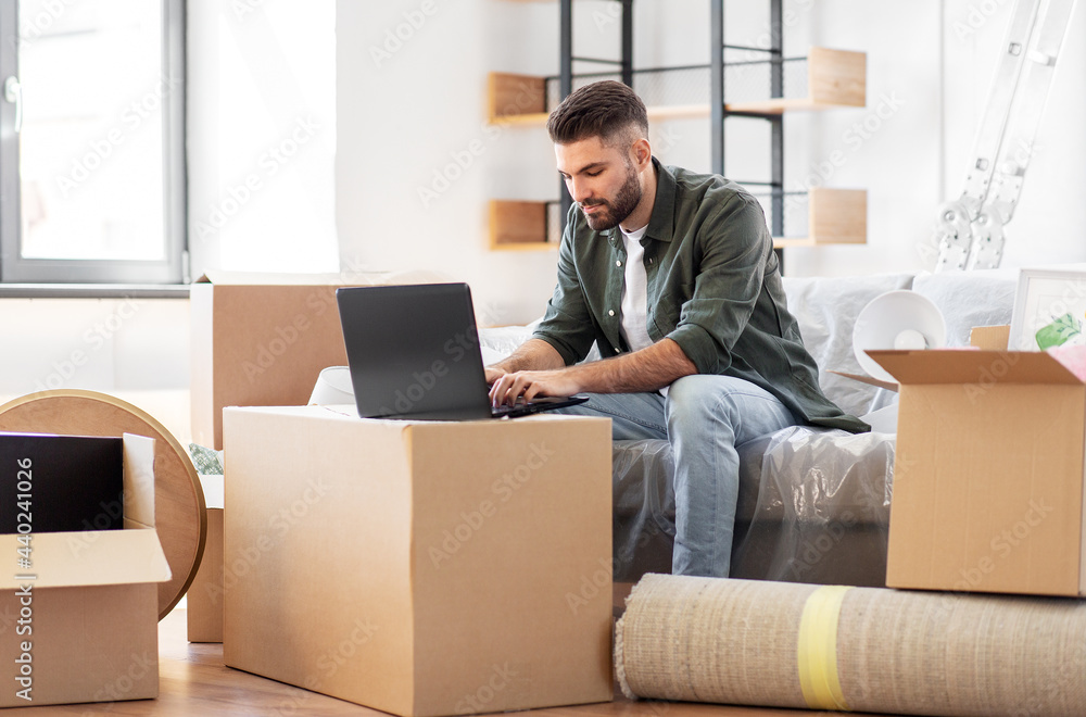 moving, people and real estate concept - man with laptop computer at new home moving, people and real estate concept - man with laptop computer at new home