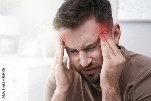 Young man suffering from migraine at home, closeup photo