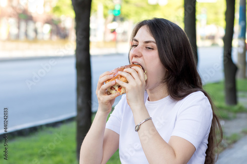 Brunette woman overeats on a burger on the street. Gluttony  excess calories  and bulimia.