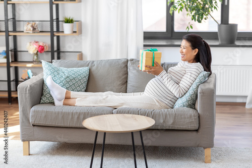 pregnancy, holidays and people concept - happy smiling pregnant asian woman with gift box sitting on sofa at home