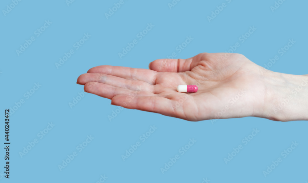 Female hand holding pill on blue background. Close-up. Place for text.