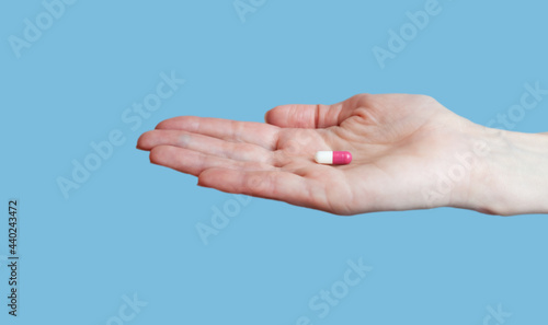 Female hand holding pill on blue background. Close-up. Place for text.