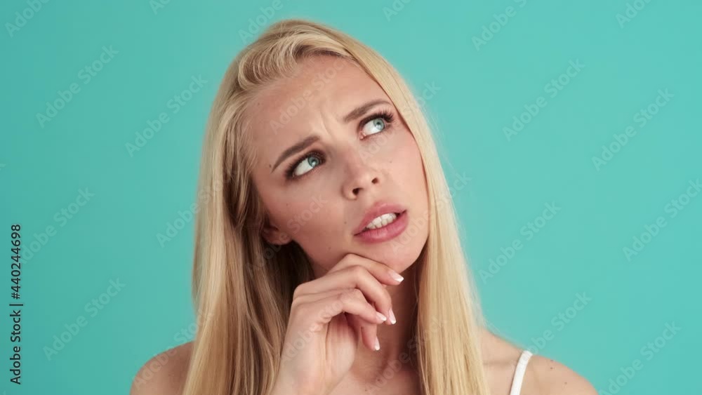 A serious young blonde woman is posing standing isolated over blue wall in the studio A serious young blonde woman is posing standing isolated over blue wall in the studio