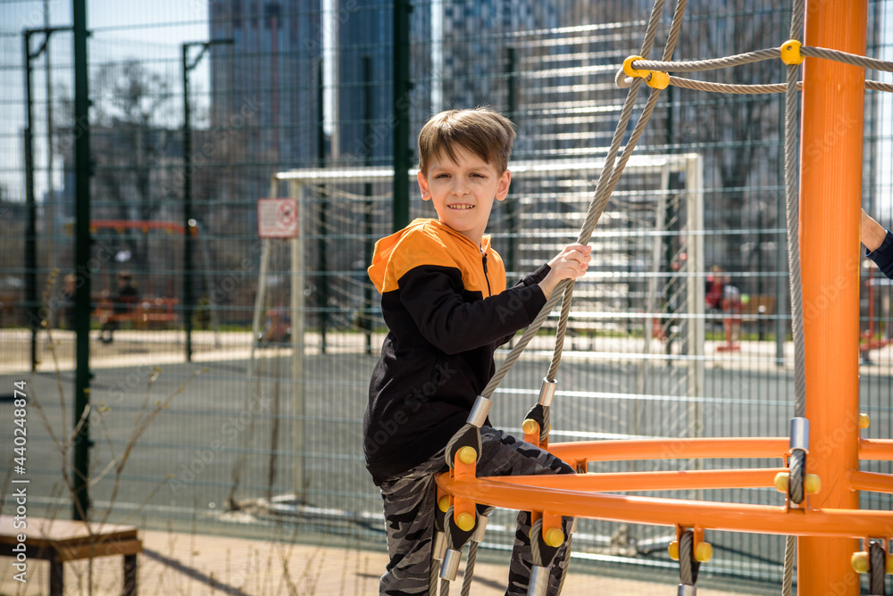 Cute boy is climbing on the playground in the schoolyard. He has a very happy face and enjoy this adventure sports alone outdoor. Warm sunny day