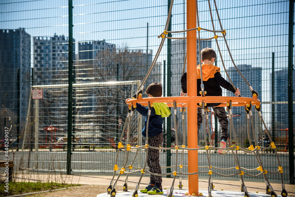 Two young boy active little child playing climbing at spring metal playground his hand to exercise at outdoor. Warm sunny day. Friendship concept