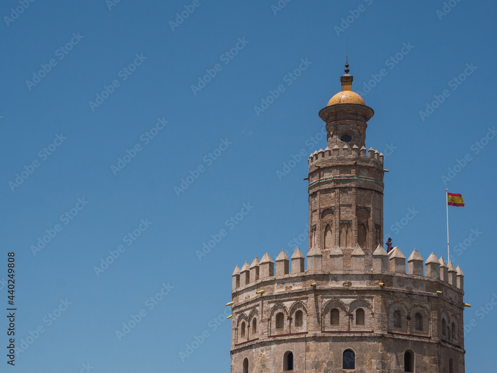 View of Torre del Oro (Tower of Gold) with spanish flag and blue sky and copy space