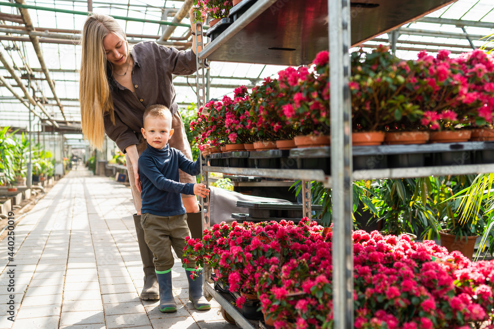 Woman greenhouse worker and her son pulling a cart with flowers Woman greenhouse worker and her son pulling a cart with flowers