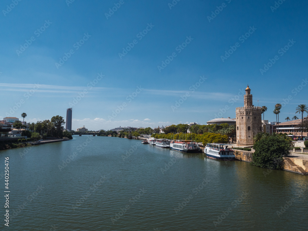 View from the Guadalquivir river of the Torre Sevilla (the city's first skyscraper) and the Torre del Oro (Tower of Gold) with blue sky of summer