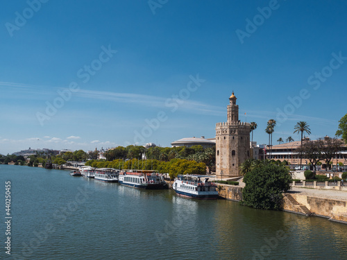 Torre del Oro (tower of gold) next to the Guadalquivir river with boats and blue sky