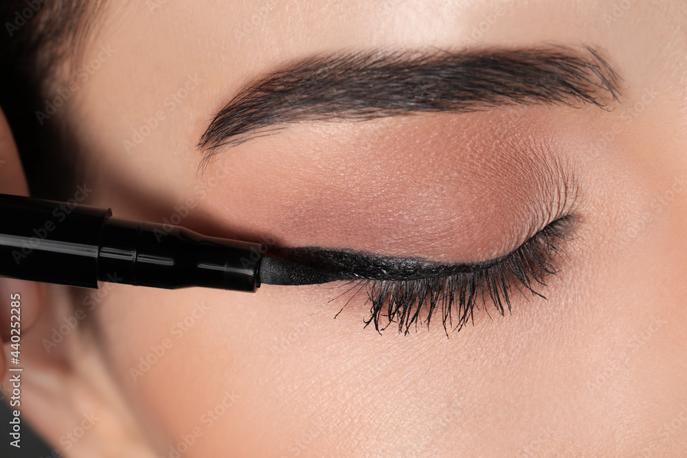 Beautiful woman applying black eyeliner, closeup view