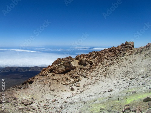 The rocky peak of the Teide volcano with yellow sulfur emissions, a view of the land covered with clouds