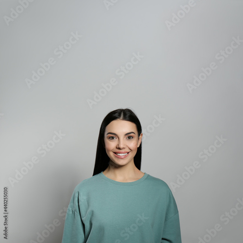Portrait of happy young woman with beautiful black hair and charming smile on light grey background
