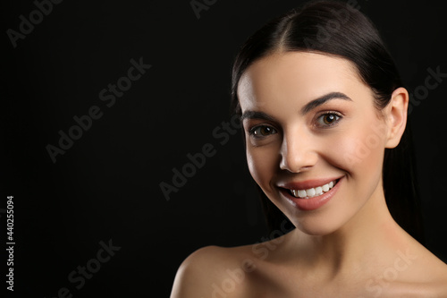 Portrait of happy young woman with beautiful black hair and charming smile on dark background, space for text