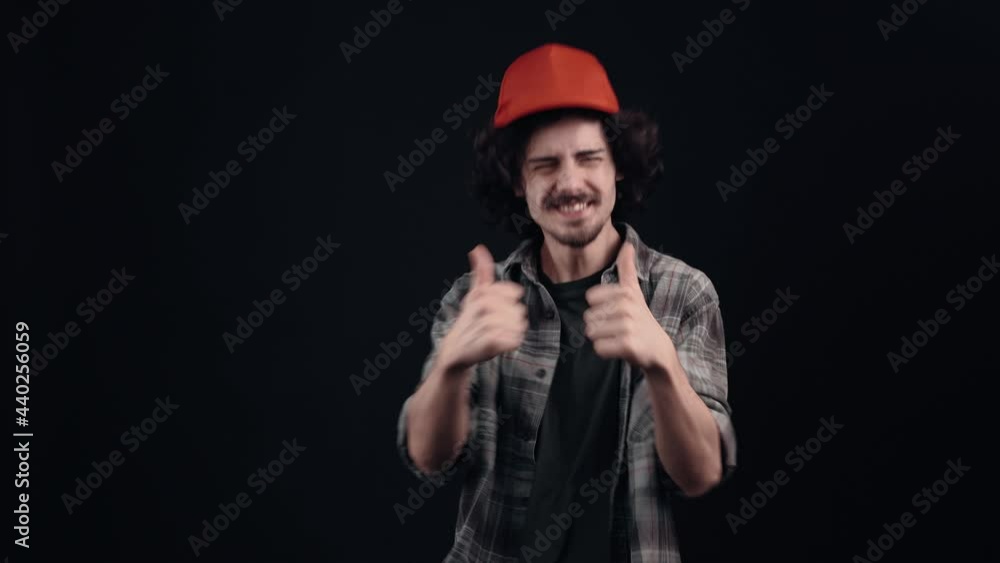 The charismatic young man with the red cap points with his index finger to one side says wow and smiles happily and in amazement. Isolated on black background. The concept of life. People's emotions The charismatic young man with the red cap points with his index finger to one side says wow and smiles happily and in amazement. Isolated on black background. The concept of life. People's emotions