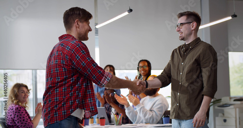 Young businessmen handshake on team meeting with group of people applauding in modern startup office