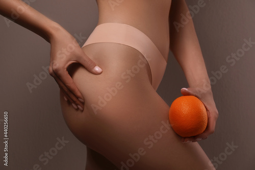 Closeup view of slim woman in underwear with orange on beige background. Cellulite problem concept