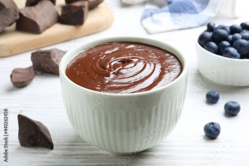 Delicious chocolate cream and blueberries on white wooden table  closeup