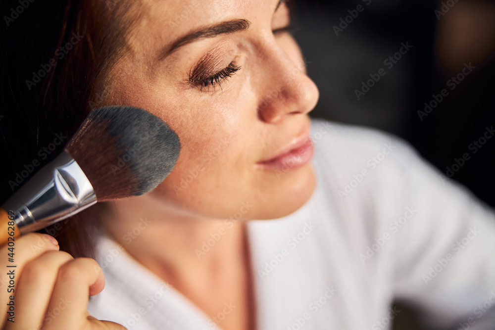 Portrait of pretty female putting blushes on cheeks Portrait of pretty female putting blushes on cheeks