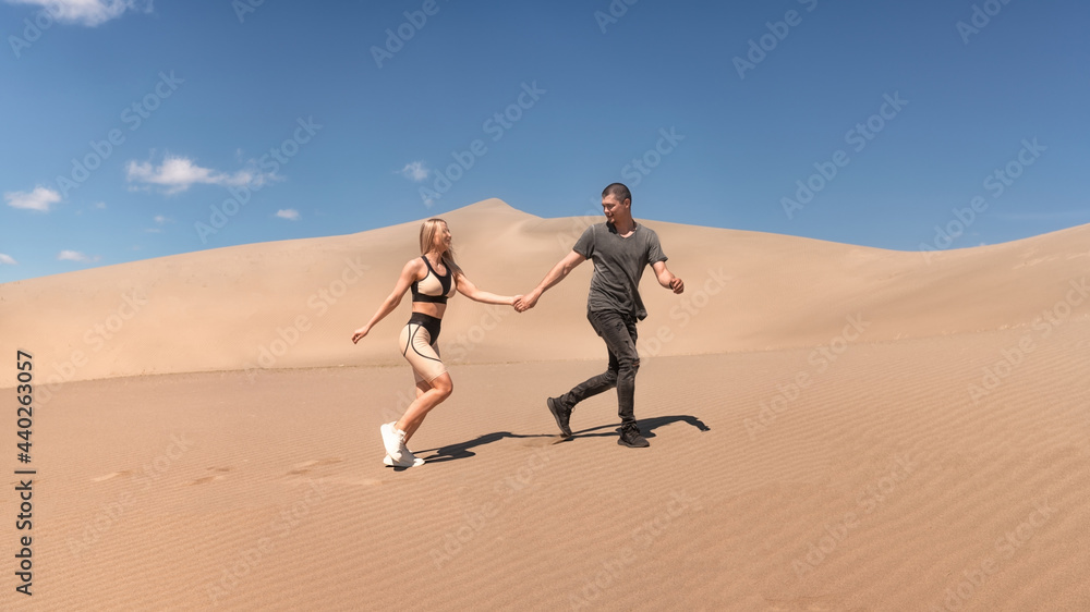 Fototapeta premium A loving couple walks down the desert dunes. A guy and a girl run through the sand. Sunny day blue sky.