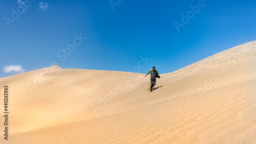 A man walks down the dunes of the desert. The guy runs on the sand. Sunny day blue sky.