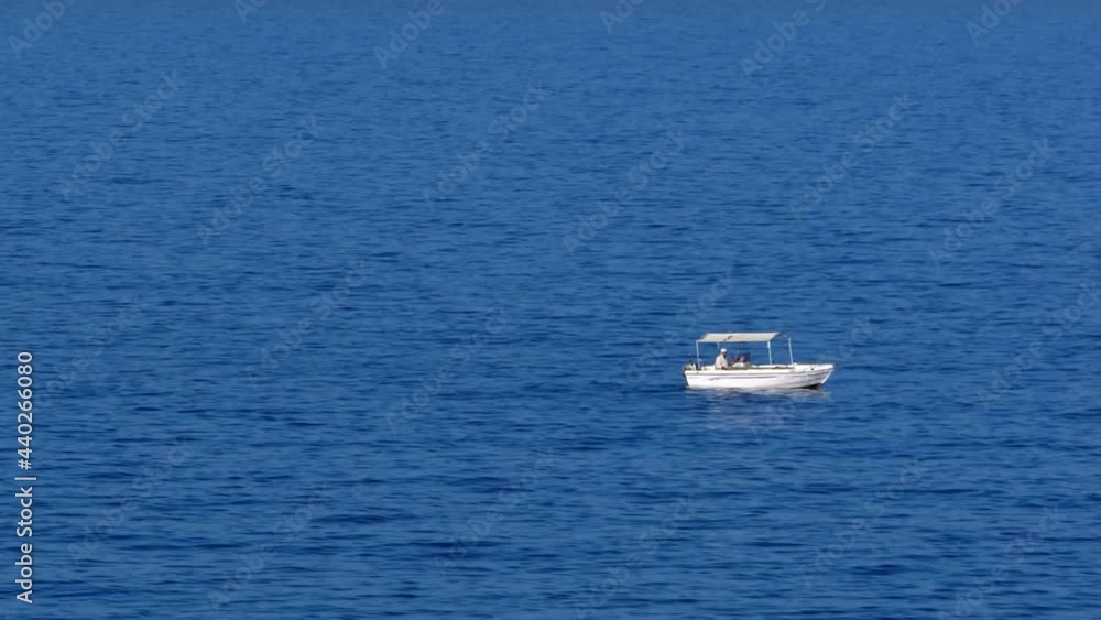 Small white fishing boat with a single fisherman on board, alone in the Mediterranean Sea off the coastline of Crete Small white fishing boat with a single fisherman on board, alone in the Mediterranean Sea off the coastline of Crete
