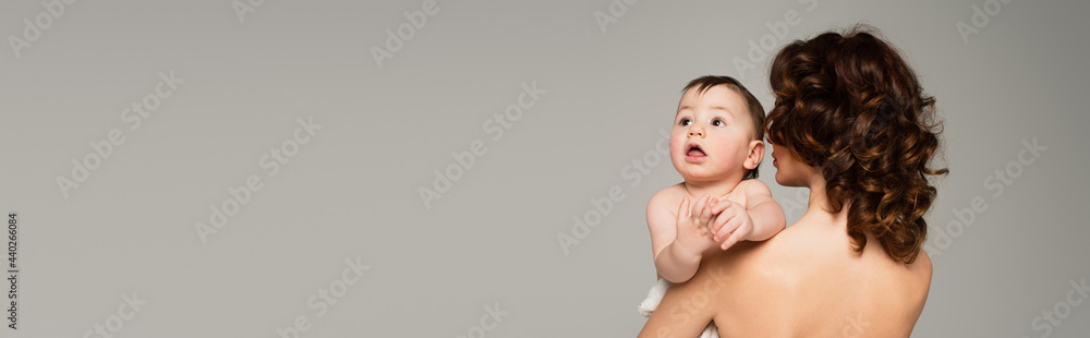 curly mother with bare shoulders holding in arms son isolated on grey, banner curly mother with bare shoulders holding in arms son isolated on grey, banner