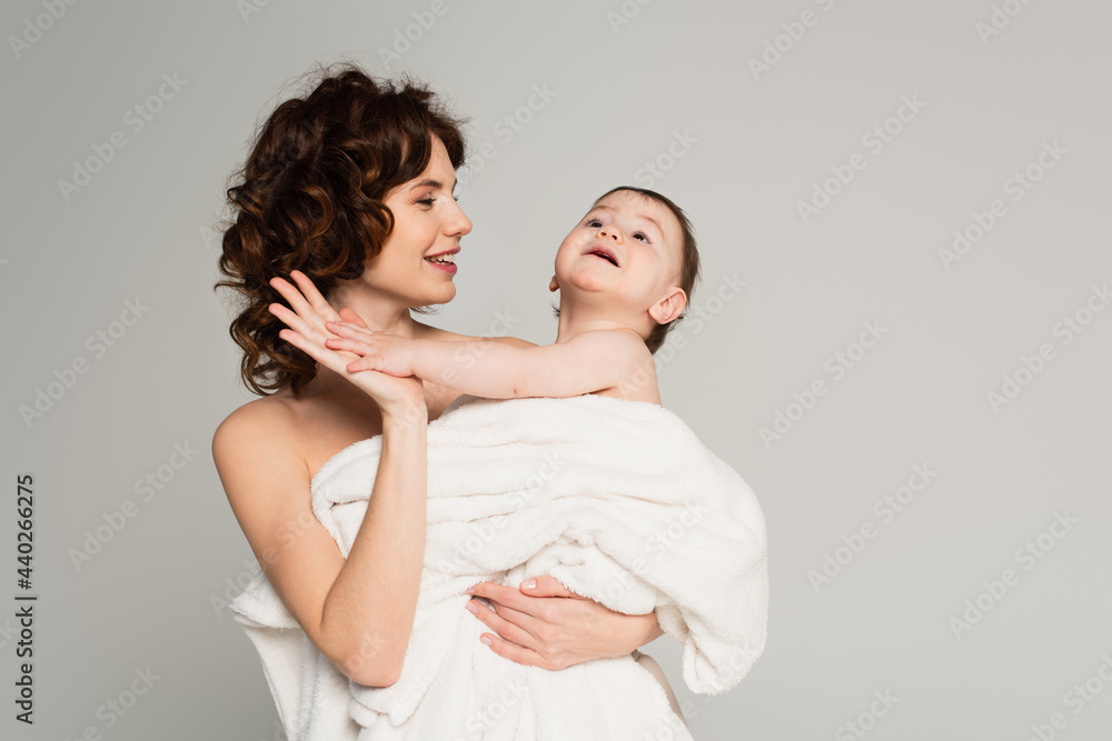 positive mother with bare shoulders giving high five to baby boy wrapped in towel isolated on grey positive mother with bare shoulders giving high five to baby boy wrapped in towel isolated on grey