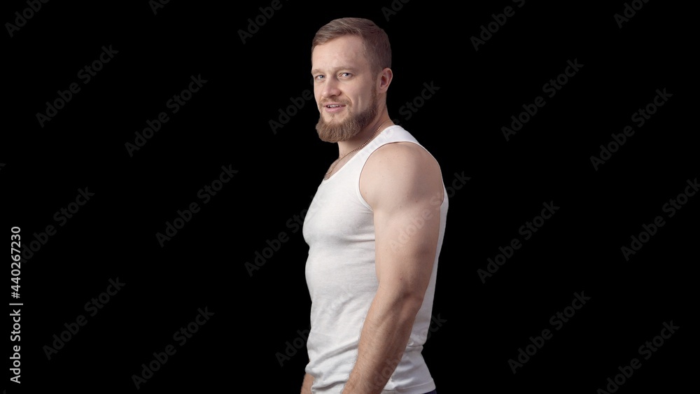 Naklejka premium Caucasian sporty man stands sideways in a tank top on a black background. One man is a model. High quality photo