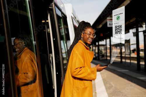 Smiling woman leaving bus at bus station with Covid-19 vaccine certificate on cell phone photo