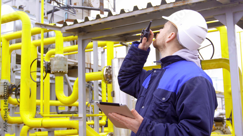 Engineer holding a tablet, talking on walkie-talkie in modern industrial factory © nimito