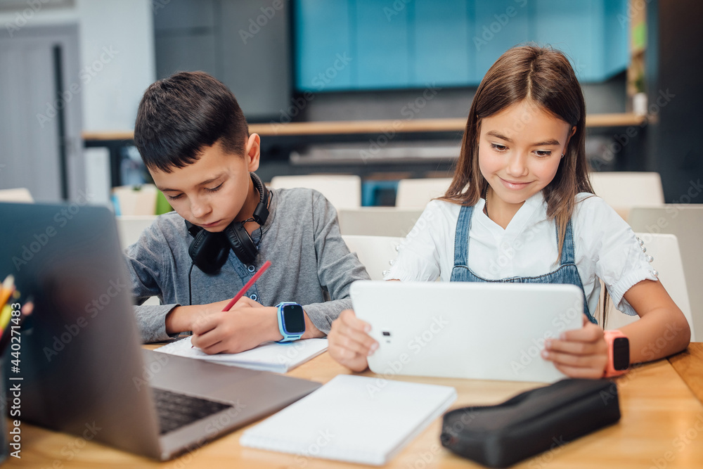 Two small friends writing homework , using smart digital tablet at modern blue classroom.
