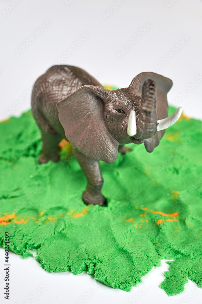 Obraz premium Toy elephant on green kinetic sand, children's games.