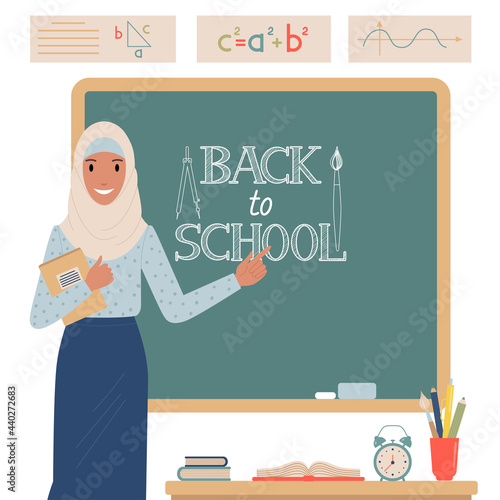 Muslim teacher stands near the school blackboard.
