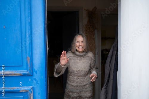 Smiling senior woman standing in doorway and waving photo