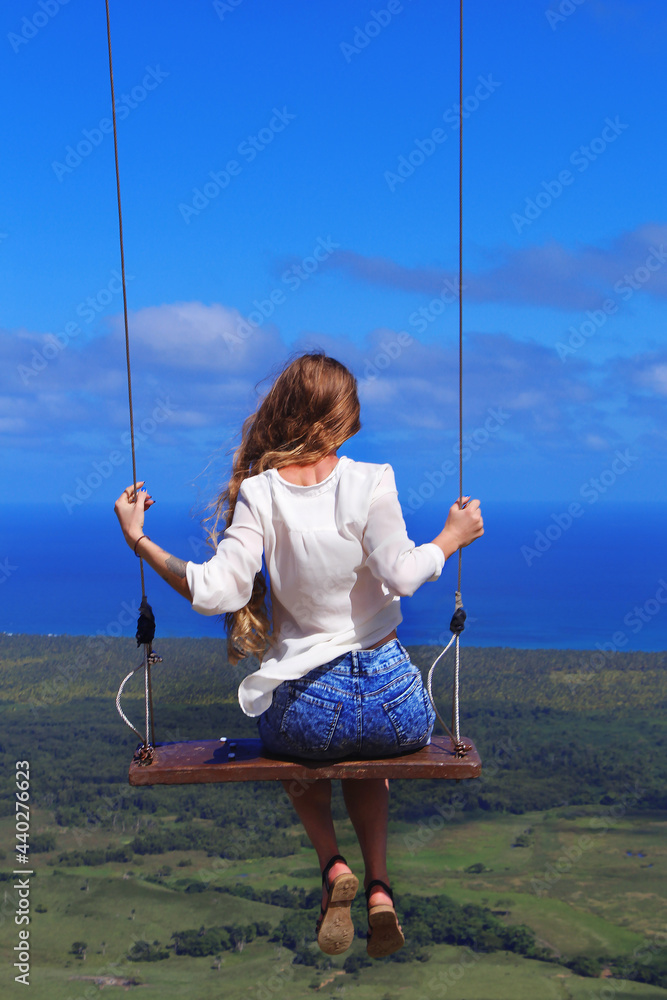 happy smiling girl with long hair in a seesaw on top of a hill on the coast of the Atlantic Ocean