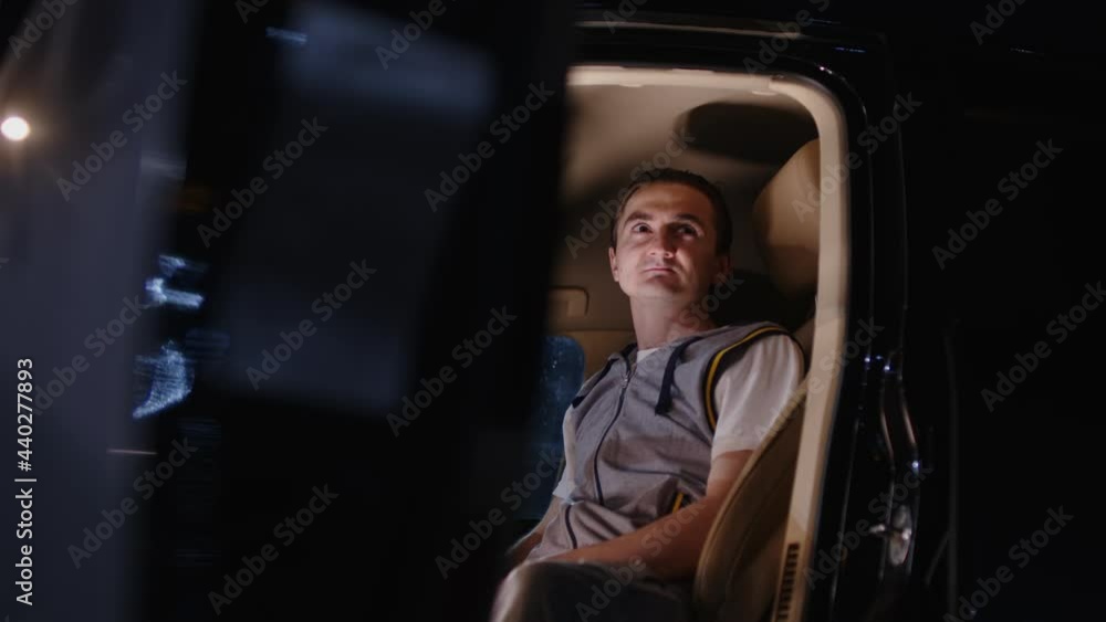 Close up of young man sitting in car behind wheel and looking away in nighttime. Tired guy resting in automobile from driving and looking away thoughtfully. Close up of young man sitting in car behind wheel and looking away in nighttime. Tired guy resting in automobile from driving and looking away thoughtfully.