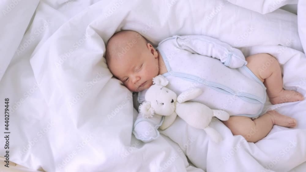 cute little newborn baby boy sleeping in the nursery on the white cotton bed at home with a toy in hand, healthy baby sleep cute little newborn baby boy sleeping in the nursery on the white cotton bed at home with a toy in hand, healthy baby sleep