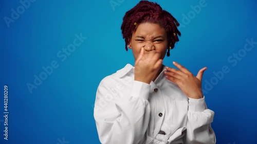 Afro woman in white shirt close nose because of a bad stinky smell, blue background