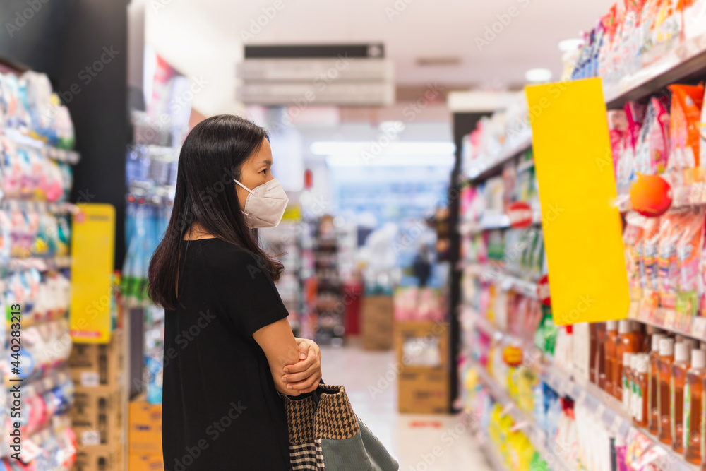 Asian woman with protective mask choosing food in supermarket during coronavirus pandemic.