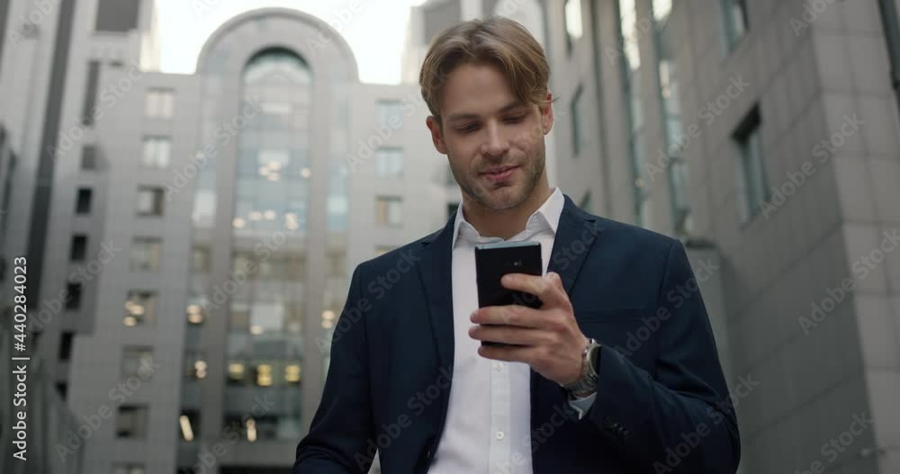 Smiling Startup Businessman with Smartphone standing in the Financial District. Handsome Young Entrepreneur chatting using Social Networks. Typing Message. Mobile Phone. Classic Suit. Browsing. Smiling Startup Businessman with Smartphone standing in the Financial District. Handsome Young Entrepreneur chatting using Social Networks. Typing Message. Mobile Phone. Classic Suit. Browsing.
