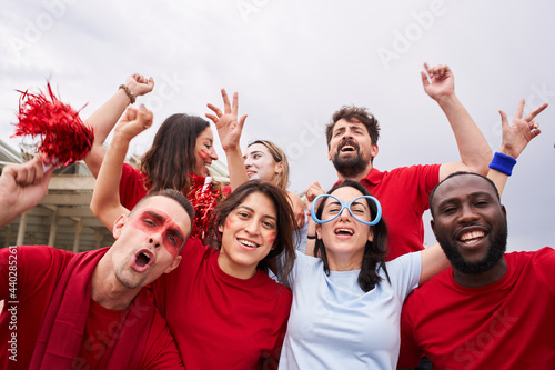 Group of supporters of a soccer team watching a game in the stands wearing blue t-shirts. Men and women euphorically celebrate a goal looking at camera. Group of different races support their team. © CarlosBarquero