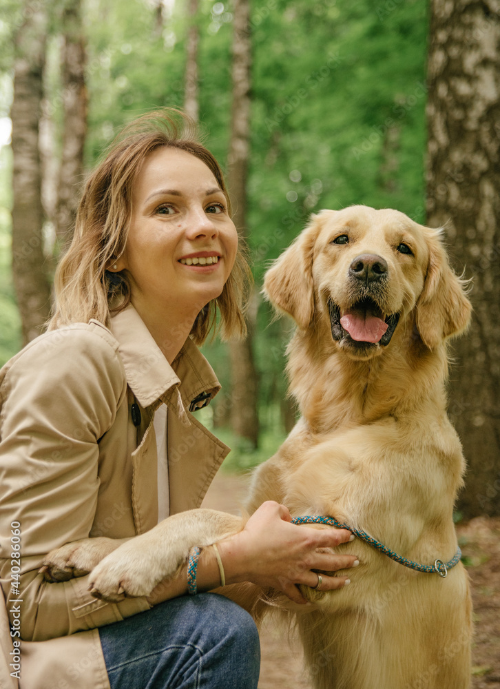 The mistress girl in the forest on the path hugs her dog of the golden retriever breed