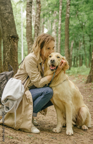 The mistress girl in the forest on the path hugs her dog of the golden retriever breed