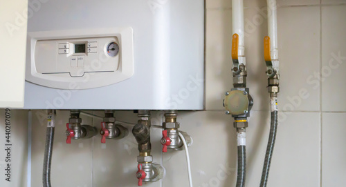 A gas double-circuit boiler is installed in the apartment. Autonomous heating boiler with a control panel, buttons, a display with temperature readings and red valves on pipes in a home kitchen.