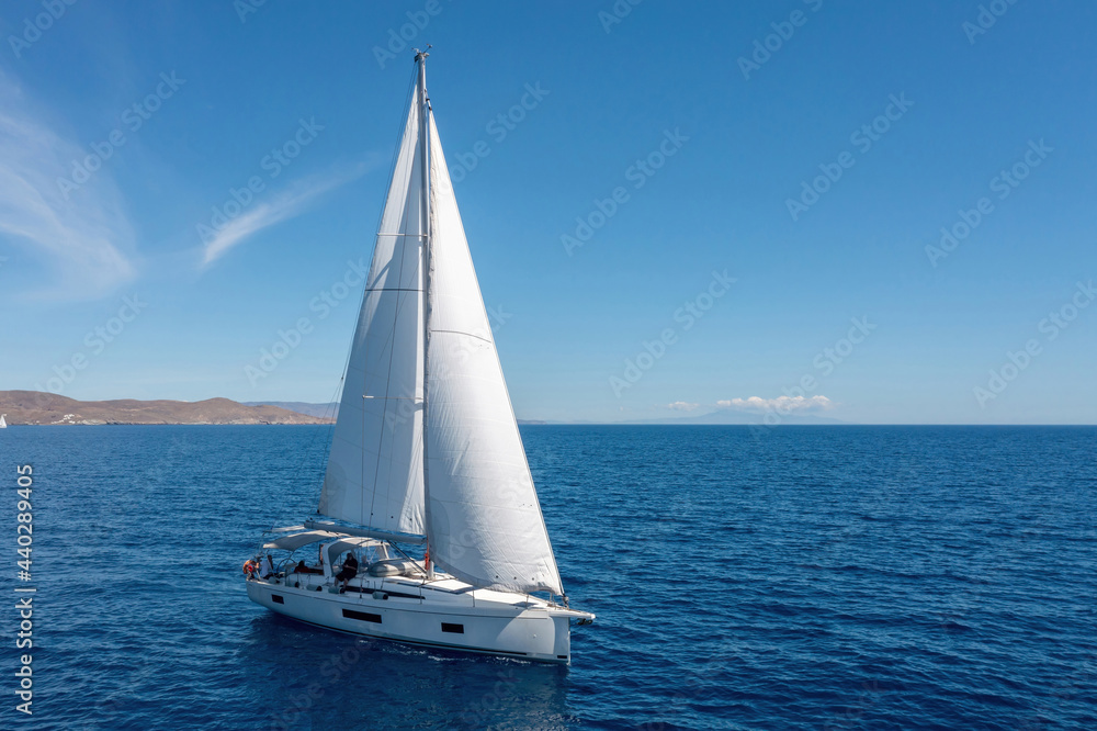 Sailing boat with open white sails, blue sky and rippled sea background