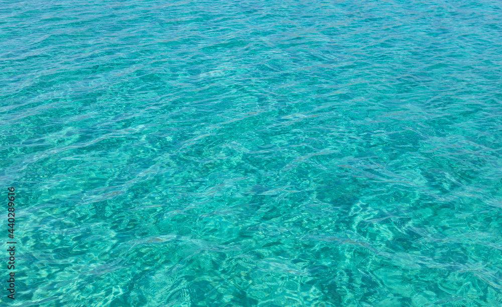 Sea surface turquoise blue color background, some reflections. Calm crystal clear water with small ripples.